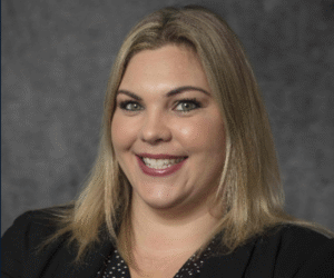 Professional headshot of a smiling woman with straight blonde hair, kind green eyes, wearing a black blazer.