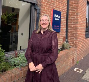 claire long stood outside our office. it is sunny, she is smiling.